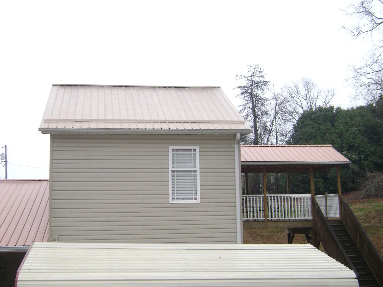 Tan metal roofs on a two story addition and attached porch, from a Roof Replacement job in Fountain